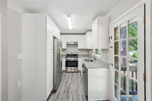 kitchen featuring appliances with stainless steel finishes, a sink, light stone countertops, white cabinetry, and light wood-type flooring