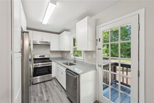 kitchen with stainless steel appliances, under cabinet range hood, a sink, light wood finished floors, and white cabinetry