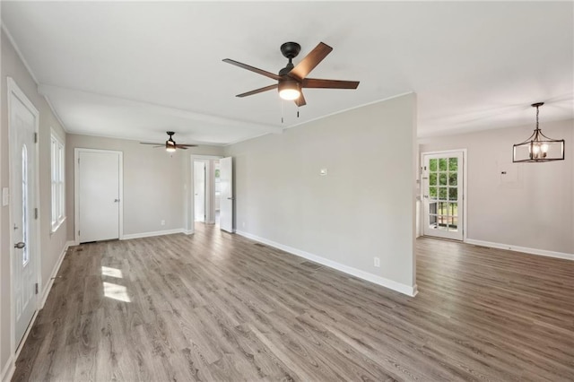 unfurnished living room featuring wood finished floors, baseboards, ceiling fan, and a chandelier