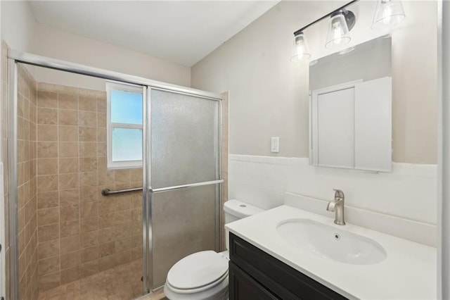 bathroom with toilet, tile walls, a shower stall, vanity, and a wainscoted wall