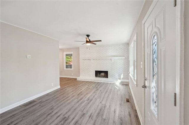 unfurnished living room featuring wood finished floors, a ceiling fan, baseboards, and a brick fireplace