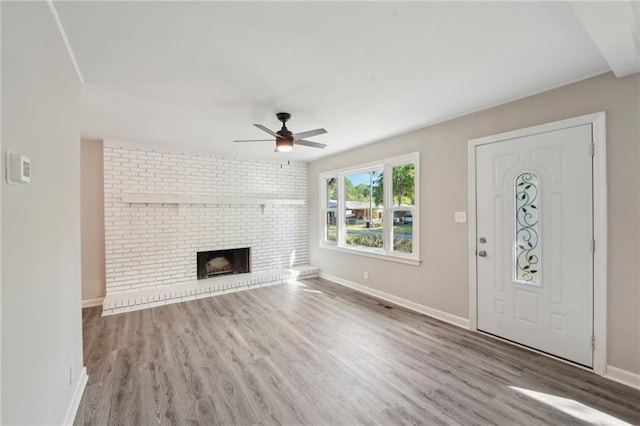 unfurnished living room with ceiling fan, wood finished floors, baseboards, and a brick fireplace