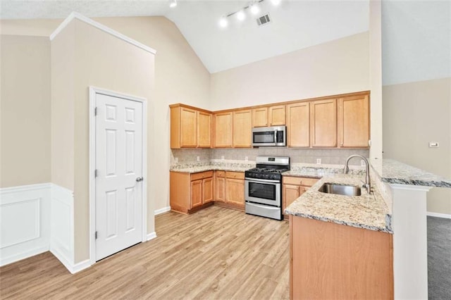 kitchen featuring visible vents, a peninsula, light stone countertops, stainless steel appliances, and a sink