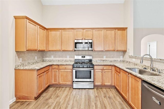 kitchen featuring light stone counters, stainless steel appliances, a sink, light wood-style floors, and tasteful backsplash