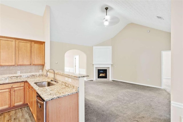 kitchen featuring light colored carpet, a peninsula, a sink, vaulted ceiling, and dishwasher