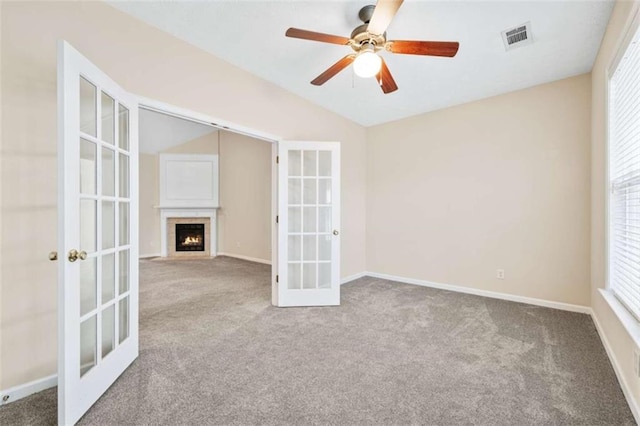 carpeted spare room featuring french doors, lofted ceiling, visible vents, a fireplace with flush hearth, and baseboards