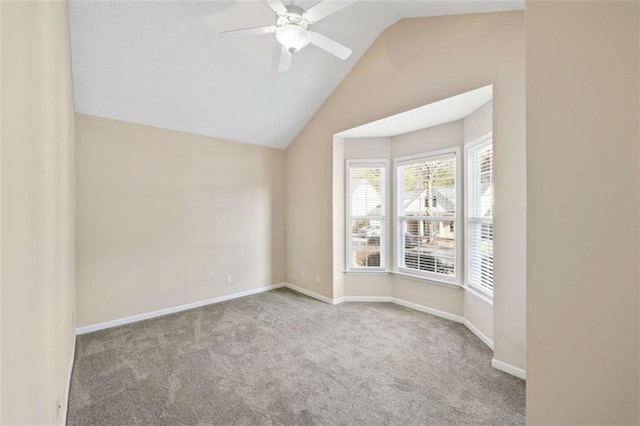 carpeted empty room featuring a ceiling fan, vaulted ceiling, and baseboards