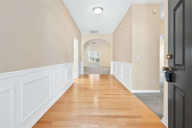 corridor featuring arched walkways, wainscoting, visible vents, and a decorative wall