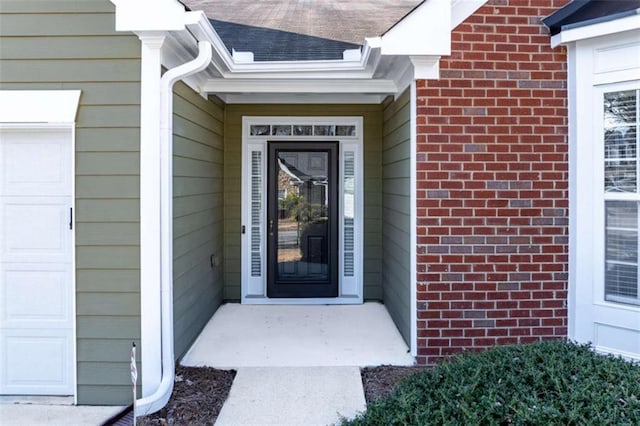 property entrance featuring a garage, brick siding, and roof with shingles