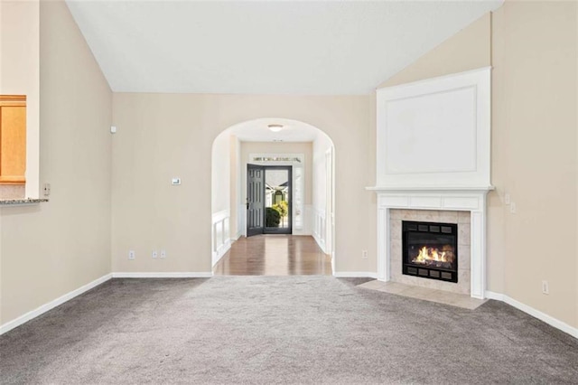 unfurnished living room featuring arched walkways, carpet flooring, vaulted ceiling, and a fireplace