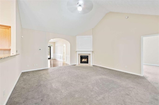 unfurnished living room with carpet floors, arched walkways, vaulted ceiling, and a tiled fireplace