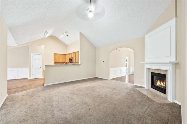 unfurnished living room with vaulted ceiling, a textured ceiling, carpet, and arched walkways