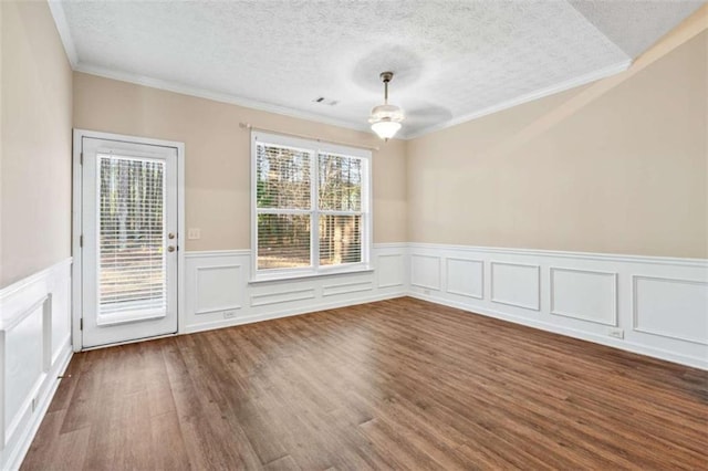 spare room with a textured ceiling, visible vents, wood finished floors, and ornamental molding