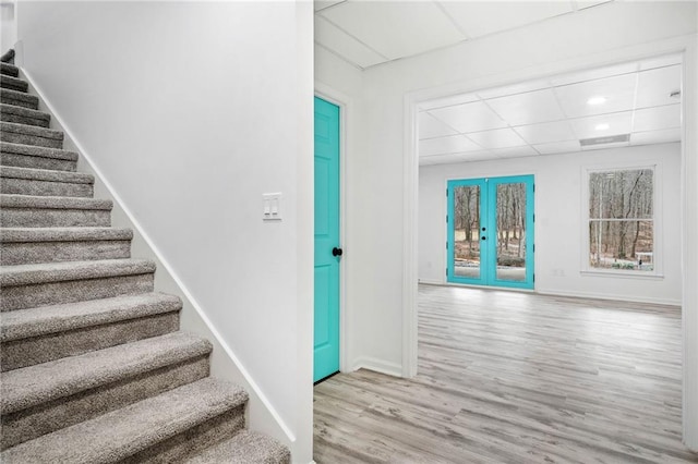 staircase featuring french doors, light hardwood / wood-style floors, and a drop ceiling