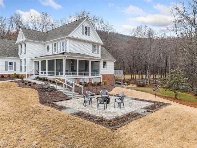 rear view of property featuring a sunroom, a lawn, a patio area, and an outdoor fire pit