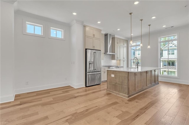 kitchen featuring wall chimney exhaust hood, sink, appliances with stainless steel finishes, an island with sink, and pendant lighting