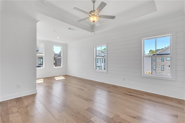 empty room featuring a tray ceiling, ceiling fan, and light wood-type flooring