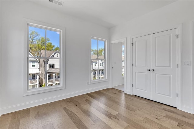 unfurnished bedroom featuring multiple windows, light hardwood / wood-style floors, and a closet