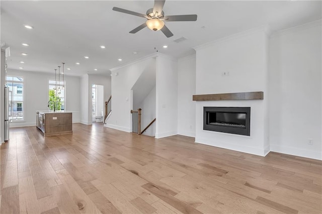 unfurnished living room with sink, crown molding, light hardwood / wood-style flooring, and ceiling fan