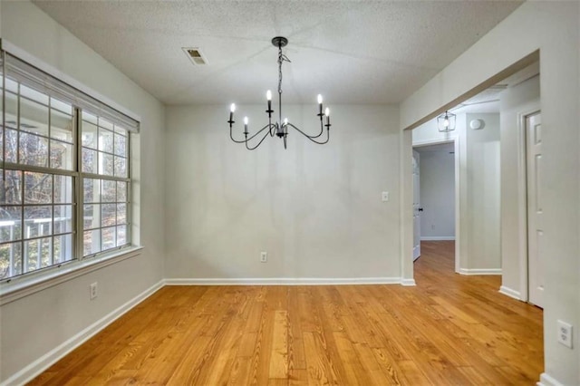 unfurnished dining area with a notable chandelier, a textured ceiling, and light hardwood / wood-style flooring