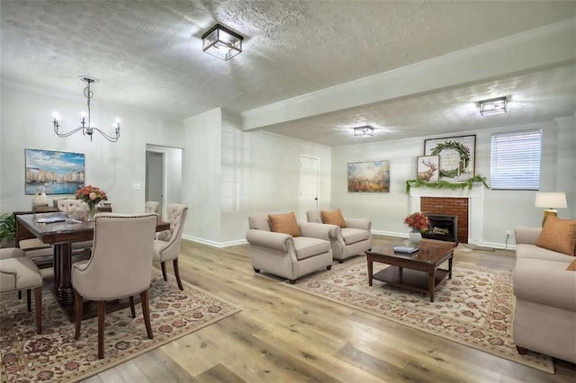 living room featuring light wood-type flooring, a brick fireplace, ornamental molding, a textured ceiling, and an inviting chandelier