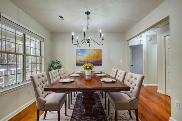 dining space featuring a healthy amount of sunlight, wood-type flooring, and an inviting chandelier