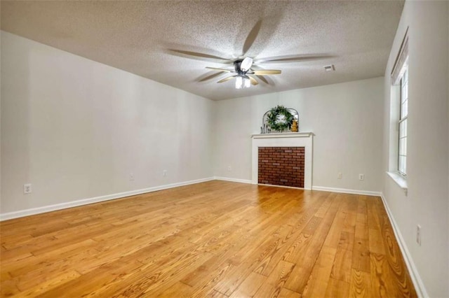 spare room featuring hardwood / wood-style floors, ceiling fan, a textured ceiling, and a brick fireplace