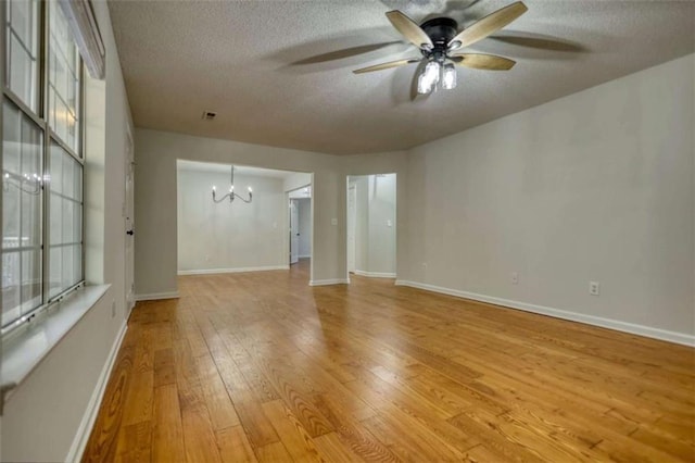 empty room featuring ceiling fan with notable chandelier, a textured ceiling, and light hardwood / wood-style floors