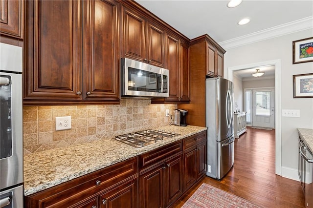 kitchen featuring backsplash, hardwood / wood-style flooring, ornamental molding, stainless steel appliances, and light stone countertops