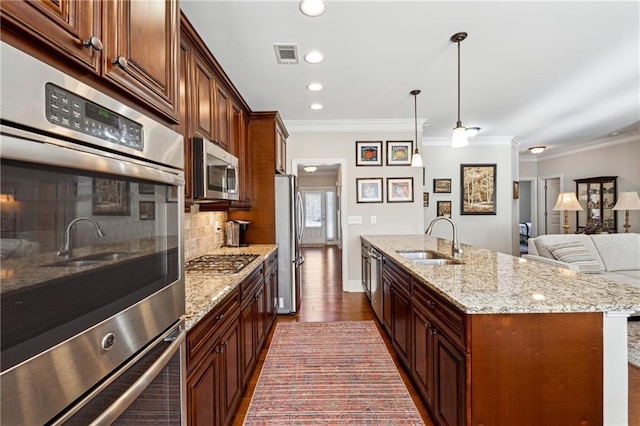 kitchen featuring appliances with stainless steel finishes, tasteful backsplash, sink, hanging light fixtures, and a kitchen island with sink