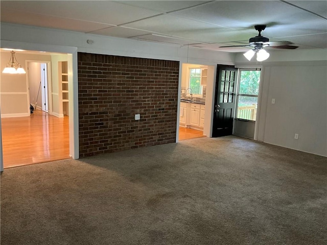 unfurnished living room with ceiling fan, hardwood / wood-style flooring, sink, and brick wall