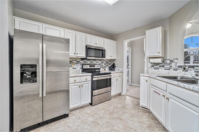 kitchen featuring appliances with stainless steel finishes, white cabinetry, a sink, and tasteful backsplash