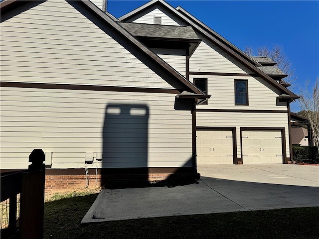 view of side of property featuring a garage, driveway, and a shingled roof