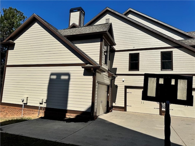 view of side of property featuring driveway, a shingled roof, a chimney, and an attached garage