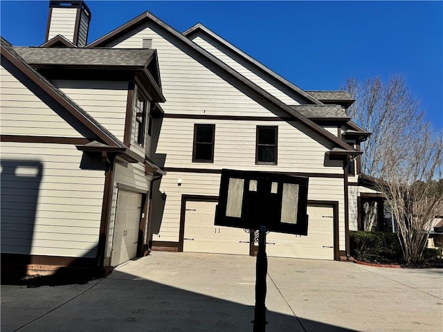 view of home's exterior with concrete driveway, roof with shingles, a chimney, and an attached garage