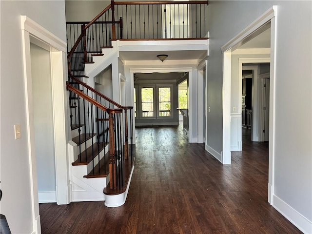 foyer entrance featuring a towering ceiling, baseboards, stairs, french doors, and dark wood-style floors