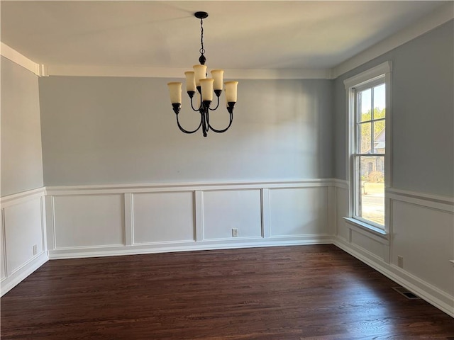 unfurnished dining area featuring visible vents, dark wood-style floors, a wainscoted wall, a chandelier, and a decorative wall