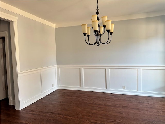 unfurnished dining area featuring dark wood-type flooring, wainscoting, and an inviting chandelier