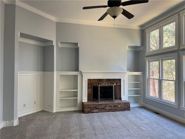 unfurnished living room featuring a wealth of natural light, a fireplace, a ceiling fan, and carpet flooring