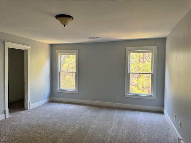 empty room featuring carpet floors, a wealth of natural light, visible vents, and baseboards