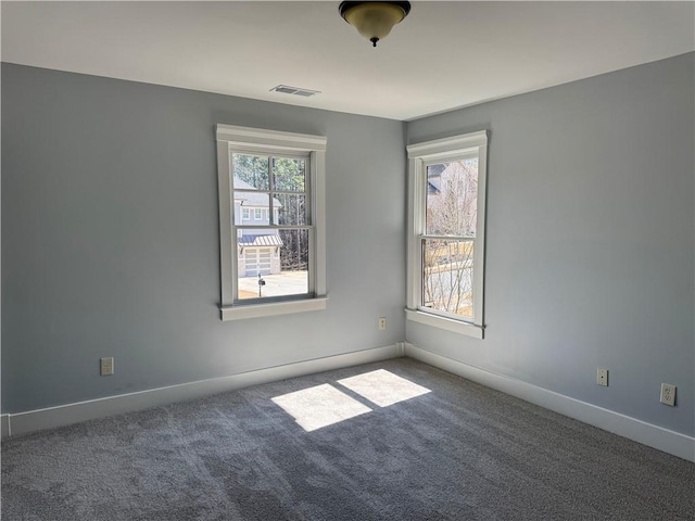 carpeted spare room featuring a wealth of natural light, visible vents, and baseboards