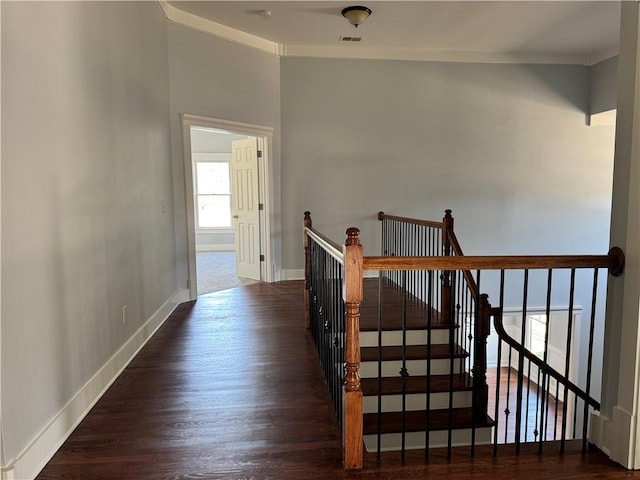 hallway with wood finished floors, visible vents, an upstairs landing, baseboards, and crown molding