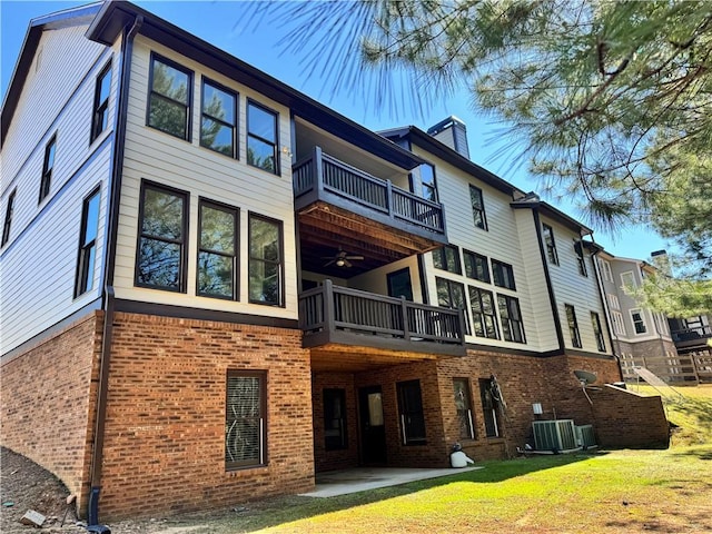 back of house featuring brick siding, a chimney, central air condition unit, a lawn, and a balcony