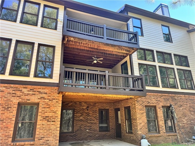 back of house featuring brick siding, a chimney, and a balcony