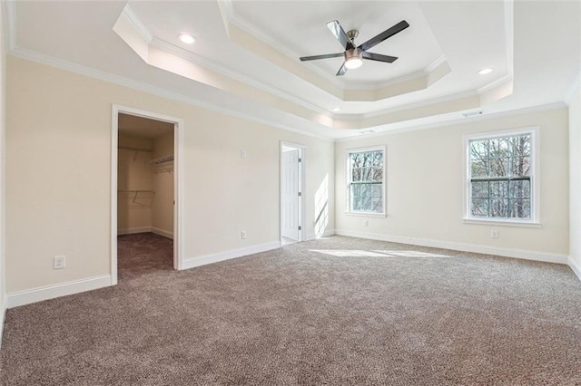 unfurnished bedroom with ceiling fan, a walk in closet, crown molding, and a tray ceiling