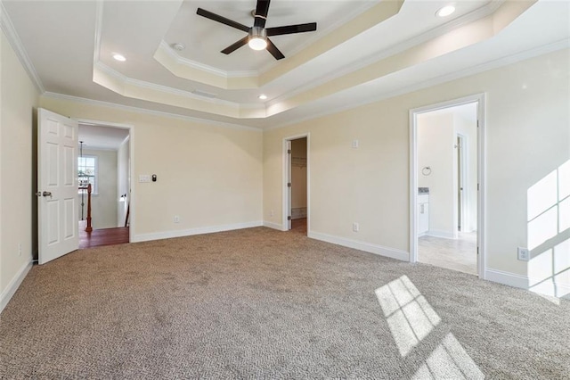 empty room with a raised ceiling, light colored carpet, ceiling fan, and crown molding