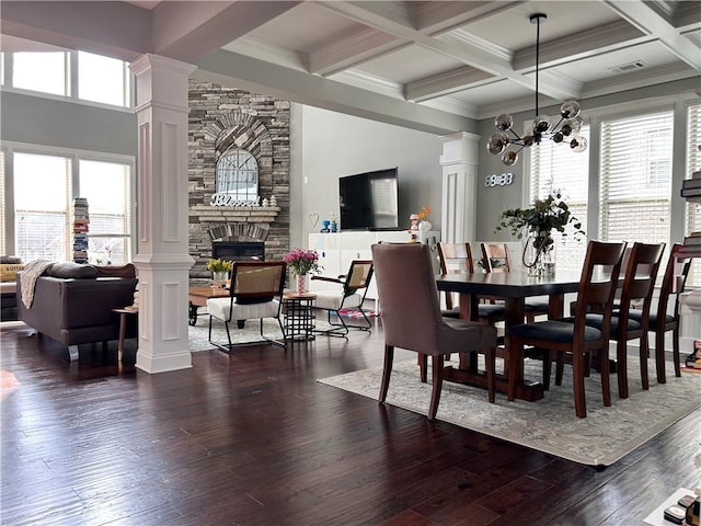 dining space with an inviting chandelier, beam ceiling, a fireplace, dark wood finished floors, and ornate columns
