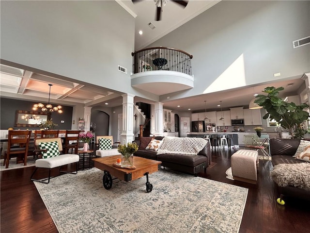 living room featuring visible vents, a towering ceiling, dark wood-style floors, ornate columns, and ceiling fan with notable chandelier