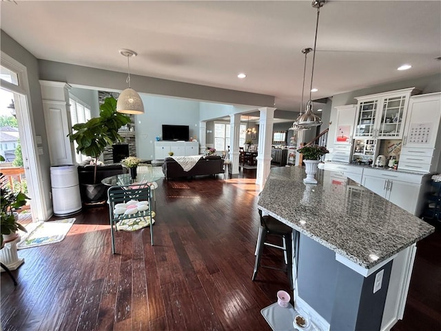 kitchen featuring white cabinets, decorative columns, a stone fireplace, and dark wood finished floors