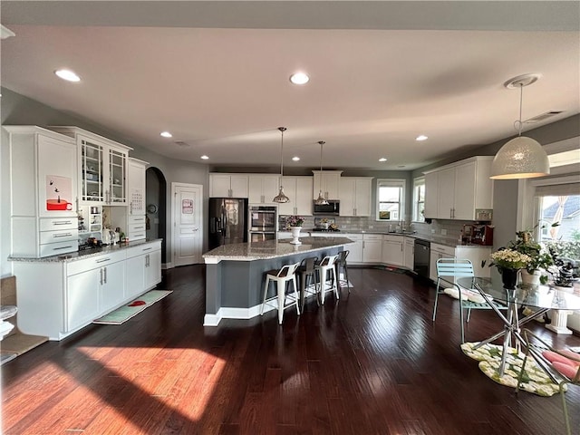 kitchen with dark wood-style floors, white cabinetry, tasteful backsplash, arched walkways, and stainless steel appliances